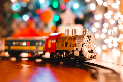 juguete locomotora de vapor vintage en el suelo bajo un árbol de Navidad decorado sobre un fondo de guirnalda de luces bokeh. photo