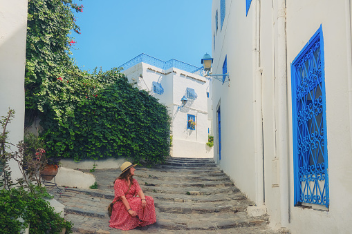 A young woman sits on street Sidi Bou Said. House with blue windows and doors with arabi ornaments, Sidi Bou Said, Tunisia, Africa
