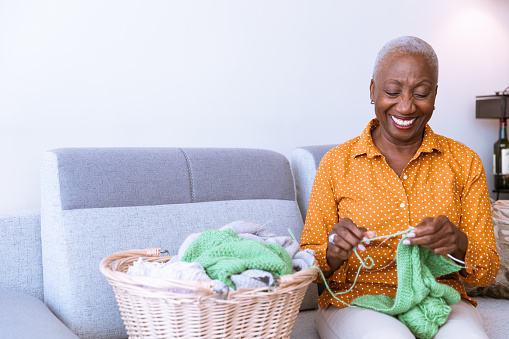 African American senior sitting on the couch and knitting at home