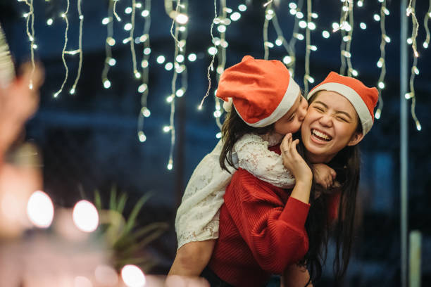 Asian chinese female carry her youngest sister and smile, youngest sister give a kiss during celebrate christmas party at roof top of house stock photo