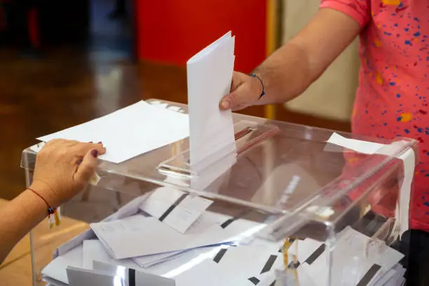 A man casts his envelope vote into a transparent plastic ballot box. Human hand voting.