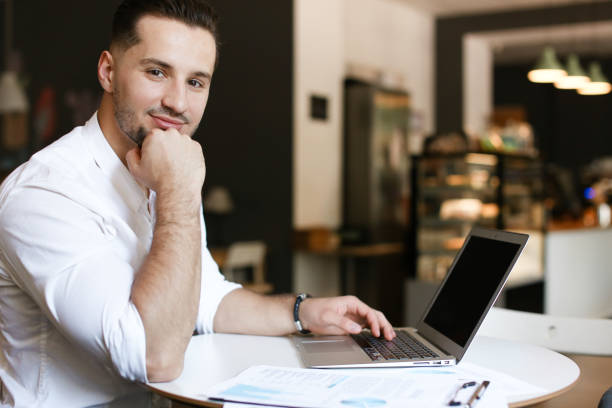 istock Young successful businessman working with documents and laptop at cafe 1184468610
