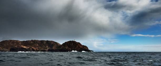 Distant lighthouse on a cliff in the sea on a stormy weather in Norway