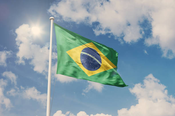 флаг бразилии, национальный символ, развевающийся на фоне облачного, голубого неба, солнечный день - бразильский флаг стоковые фото и изображения