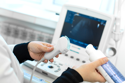 El médico prepara una máquina de ultrasonido para el diagnóstico de un paciente. El médico pone gel multimedia en un transductor de ultrasonido photo