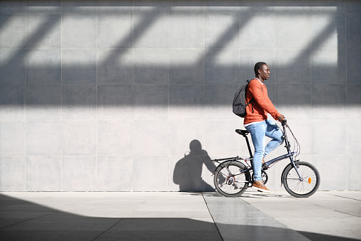 Young African Man Using a Folding Bicycle To Commute To Work. Copy Space On Wall.