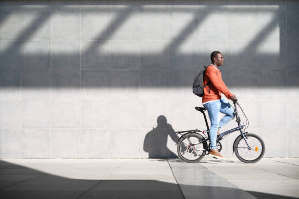African Man Riding Folding Bike For Urban Commuting Young African Man Using a Folding Bicycle To Commute To Work. Copy Space On Wall. foldable stock pictures, royalty-free photos & images