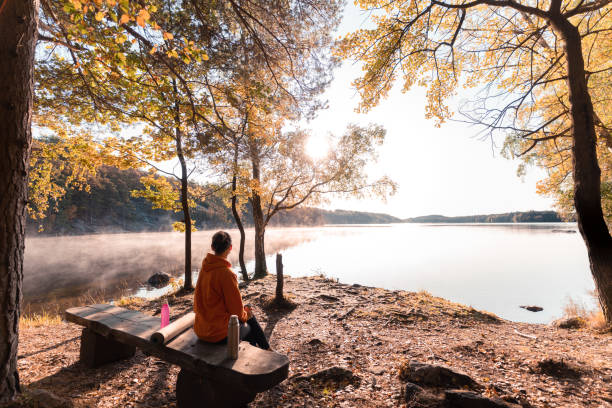 Woman drinking coffee outdoors by the lake A woman is sitting down to drink coffee after her morning yoga exercises. swedish woman stock pictures, royalty-free photos & images