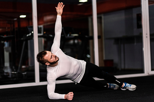 Young fitness man doing side plank exercise in fitness center