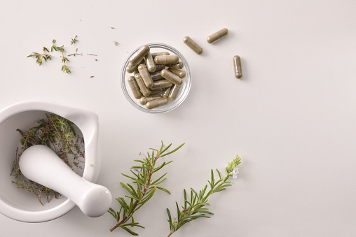 Mortar with herbs for processing natural capsules on white table. Alternative natural medicine concept. Top view. Horizontal composition.