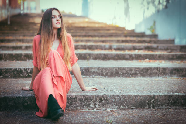 istock Beautiful gil sitting on outdoors stairs wearing red dress. 1184496601