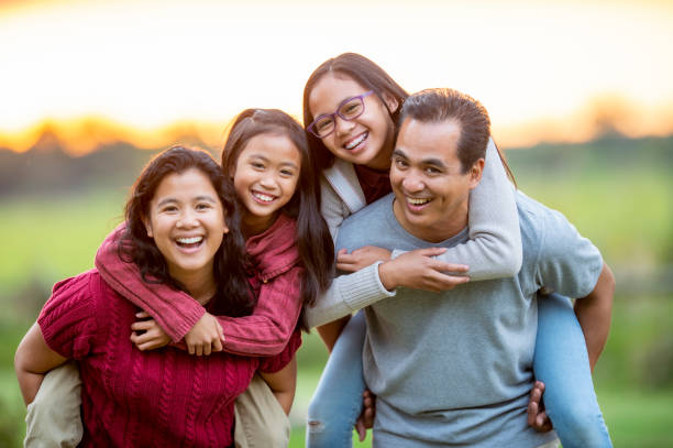 Filipino Family Piggyback Portrait Outside stock photo A small Filipino family of four spend some time close together while outside.  The Mother and Father each have an elementary school aged daughter on their back and they are smiling and enjoying a walk in the fresh air. happy filipino family stock pictures, royalty-free photos & images