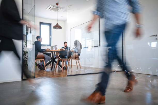 Business Colleagues in Motion Past Office Conference Room Blurred motion of male and female businesspeople walking down hallway contrasted by still and careful debate of new ideas in the conference room. business relationship photos stock pictures, royalty-free photos & images