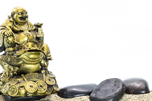 Laughing Buddha and stack of black basalt stones, on white background.