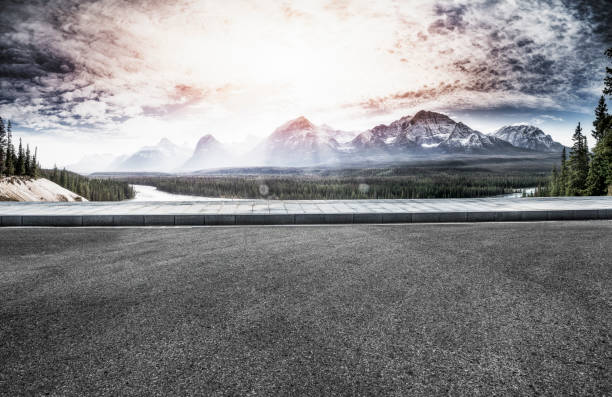 istock Empty tarmac surface with lush forests and snow-capped mountains on background 1184512282