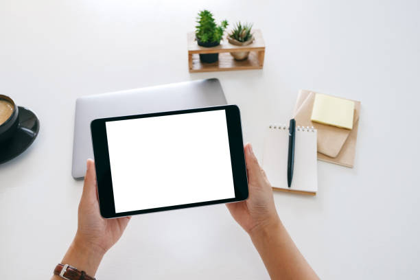 istock hands holding a tablet with blank white screen and laptop computer on wooden table in office 1184516041