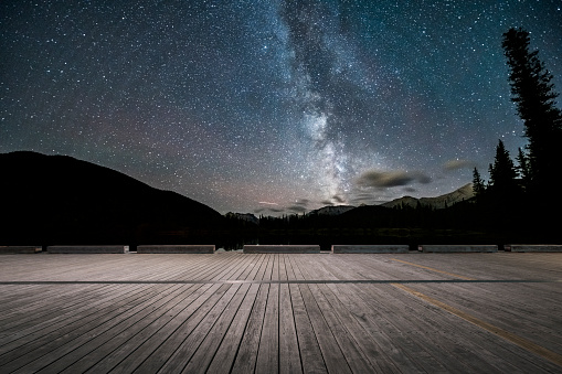 Night Sky and Stars Over Canadian Rockies With Wooden Deck On Foreground,Alberta,Canada.