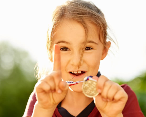 Shot of excited little girl showing her winning medal and gesturing number one hand sign
