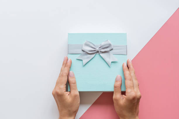 istock Abstract background with Hands holding gift box in modern style. Xmas background. Holiday mockup. Christmas greeting card. Package icon. Happy birthday. Flat lay, top view style. Shopping sale concept 1184533979
