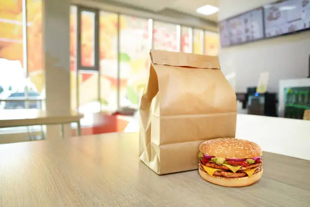 Photo of Cheeseburger and craft paper bag on wooden counter of cafe.