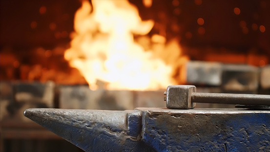 Hammer on anvil in forge on furnace with fire blur background in slow motion. Smithy workshop and workplace for manufacture of metal structures and for forging hot metal.