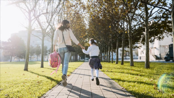 A woman and little girl in school uniform running in park, back view stock photo