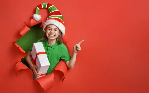 Merry Christmas! Little girl in Santa's elf costume on bright color background. Red and green.