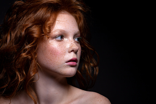 Beautiful portrait of a red-haired teenager girl. With beautiful makeup and image on a dark background.