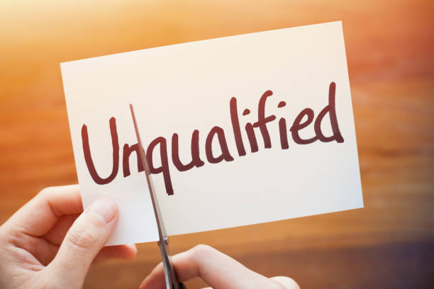 istock Cutting Out the Word Unqualified and Qualified on Paper with Scissors 1184572969