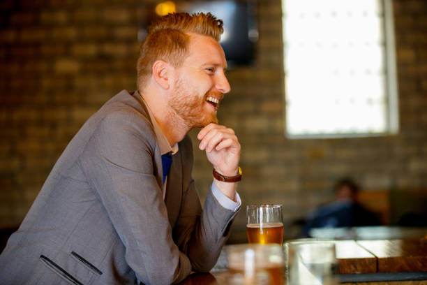 Smiling young businessman leaning on the bar counter and having beer alone after work