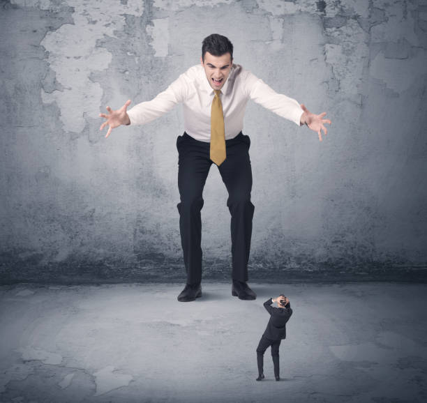 istock Big business bully looking at small coworker 1184582876