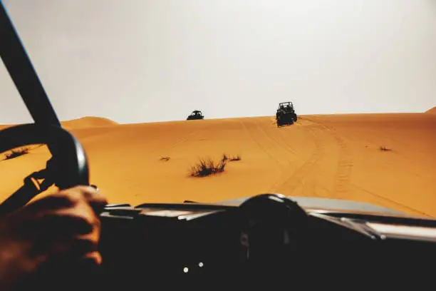 Beautiful desert landscape with off road buggies crossing dunes during rally raid adventure.