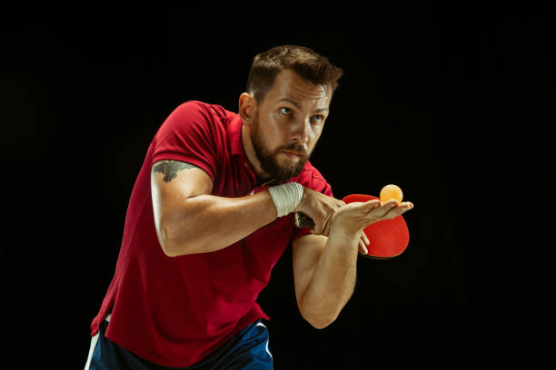 istock Young man playing table tennis on black studio background 1184585442