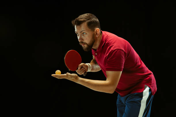 istock Young man playing table tennis on black studio background 1184585459
