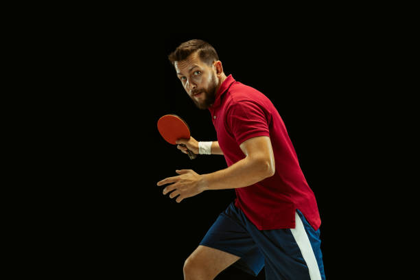 istock Young man playing table tennis on black studio background 1184585462