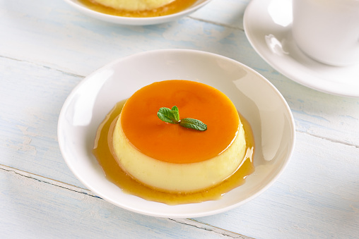 Close up of caramel custard pudding on plate over light wooden table