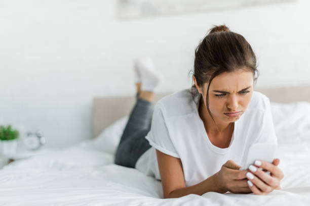 istock attractive confused girl using smartphone while lying on bed in the morning 1184595418