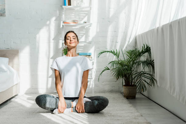 hermosa chica feliz con los ojos cerrados practicando yoga en posición de loto en el dormitorio en la mañana - fitness fotografías e imágenes de stock