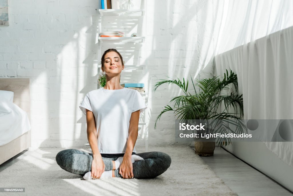 beautiful happy girl with closed eyes practicing yoga in lotus position in bedroom in the morning Yoga Stock Photo