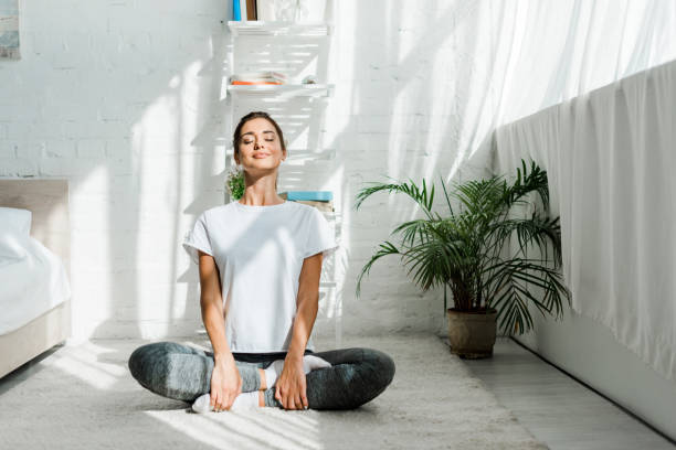 beautiful happy girl with closed eyes practicing yoga in lotus position in bedroom in the morning beautiful happy girl with closed eyes practicing yoga in lotus position in bedroom in the morning lotus position stock pictures, royalty-free photos & images