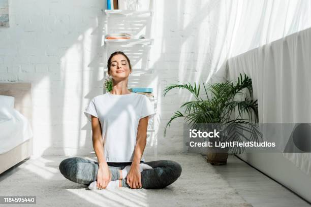 Beautiful Happy Girl With Closed Eyes Practicing Yoga In Lotus Position In Bedroom In The Morning Stock Photo - Download Image Now