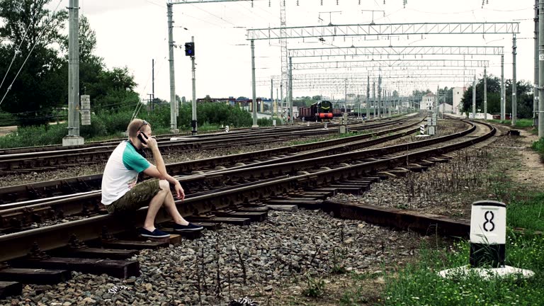 man is sitting on the railway or railroad and talkIng on the smartphone, life threatening