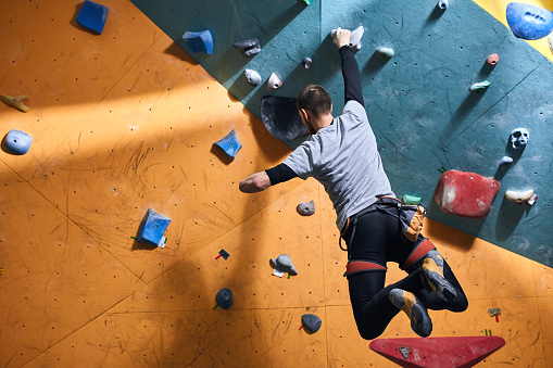 Unrecognizable powerful boulderer with physical disability hanging at climbing wall, balancing on one hand, has sporty muscled body, strong-willed, loves to overcome difficulties.