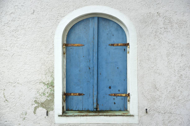istock An old weathered blue shutter closes an old window with round arches in an old wall 1184598904