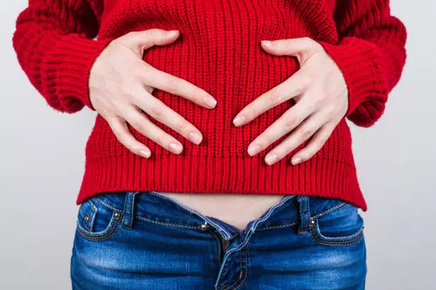 Photo of Overeating concept. Cropped close up photo of unhappy sad upset girl eating unhealthy lot of sweets dessert holding hands on red pullover feeling ill isolated grey background