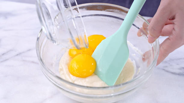 istock Mixing egg yolk into cake batter with green rubber spatula mixer tool stirring until smooth and blend well in a glass bowl. 1184602282