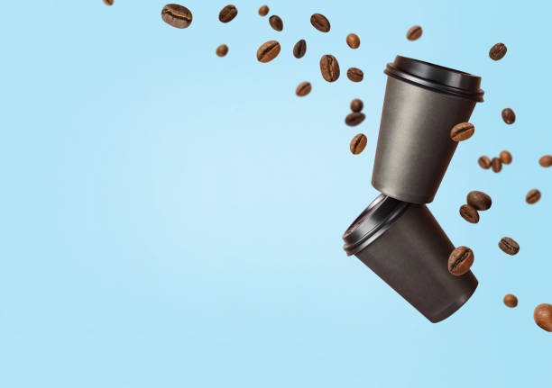 Flying coffee from a paper cups with flying coffee beans on a blue background. Coffee concept. Mockup front view. Clear plain tea take away package. Add your text.