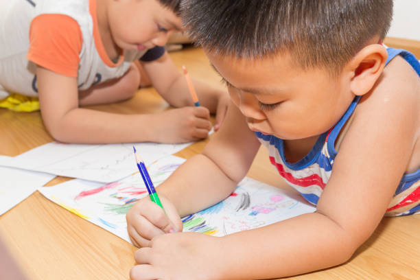 istock Cute asian boy lying on the floor coloring on paper. 1184613151
