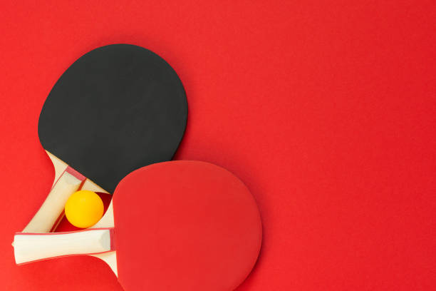 Black and red tennis ping pong rackets and orange ball isolated on a red background, sport equipment for table tennis