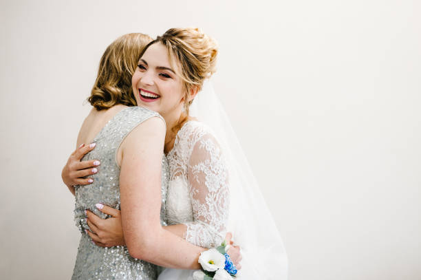 mama gratuliert der braut mit einer ehe und umarmungen. frau begrüßt. glückliche braut mit mutter auf hintergrund weiße wand zu hause. hochzeitszeremonie. nahaufnahme - bride caucasian wedding ceremony close up stock-fotos und bilder